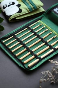 Stylish bamboo knitting needles in a green case with crochet doilies and leaves, perfect for crafters.